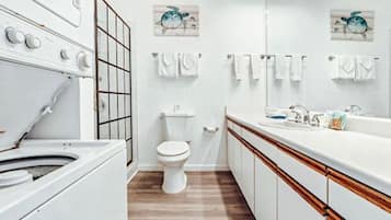 Un baño moderno con lavamanos, inodoro y un espejo grande. Hay dos toallas colgadas en la pared y un armario de madera.