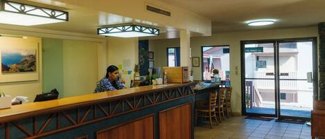 A reception area with a wooden counter, a receptionist, and a view of the outside through a glass door.