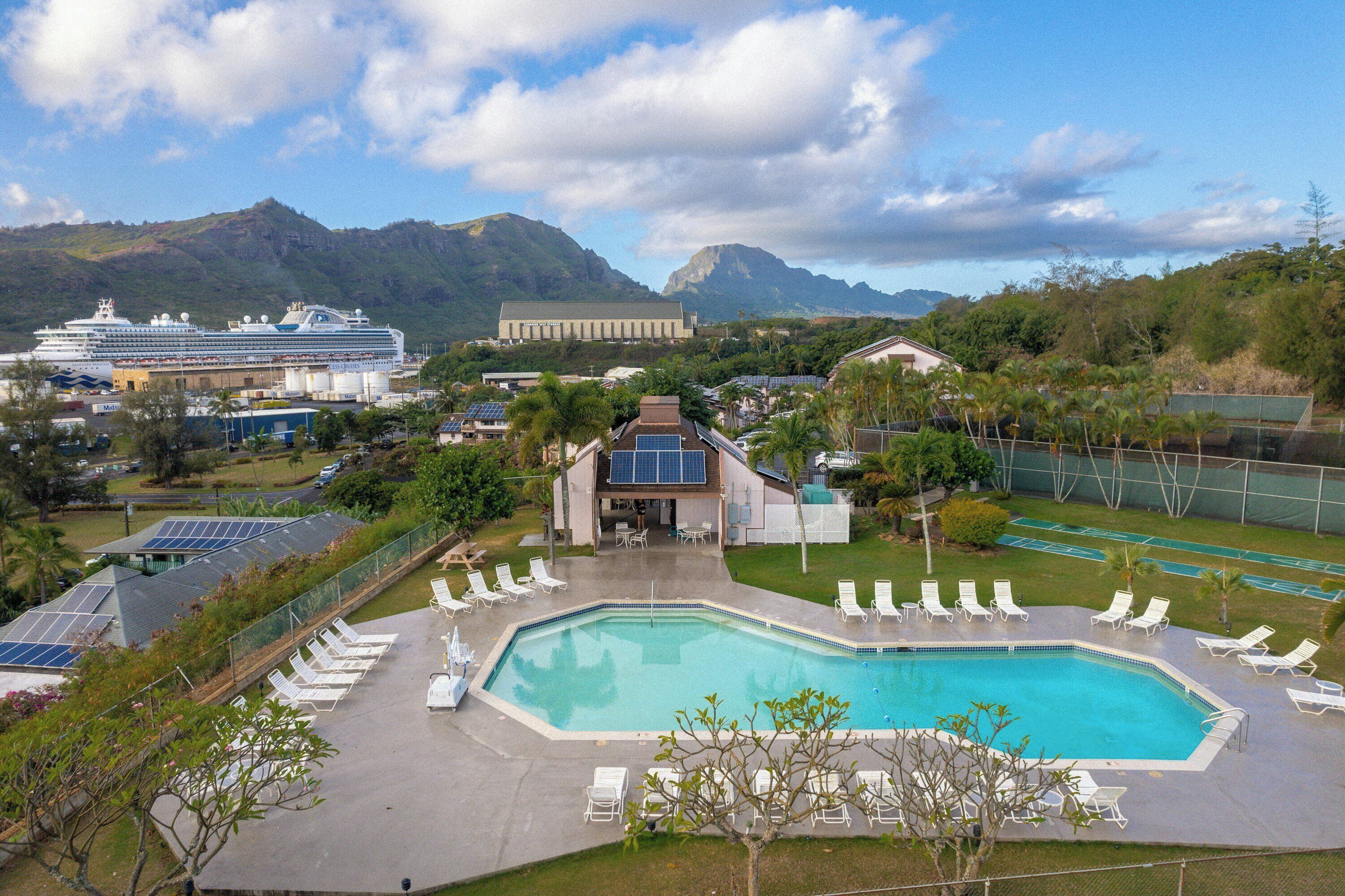 Una piscina con sillones reclinables, un edificio con paneles solares y un crucero al fondo.