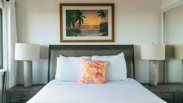 A hotel room with a bed, two bedside lamps, a framed picture of a beach scene, and a brown throw blanket.