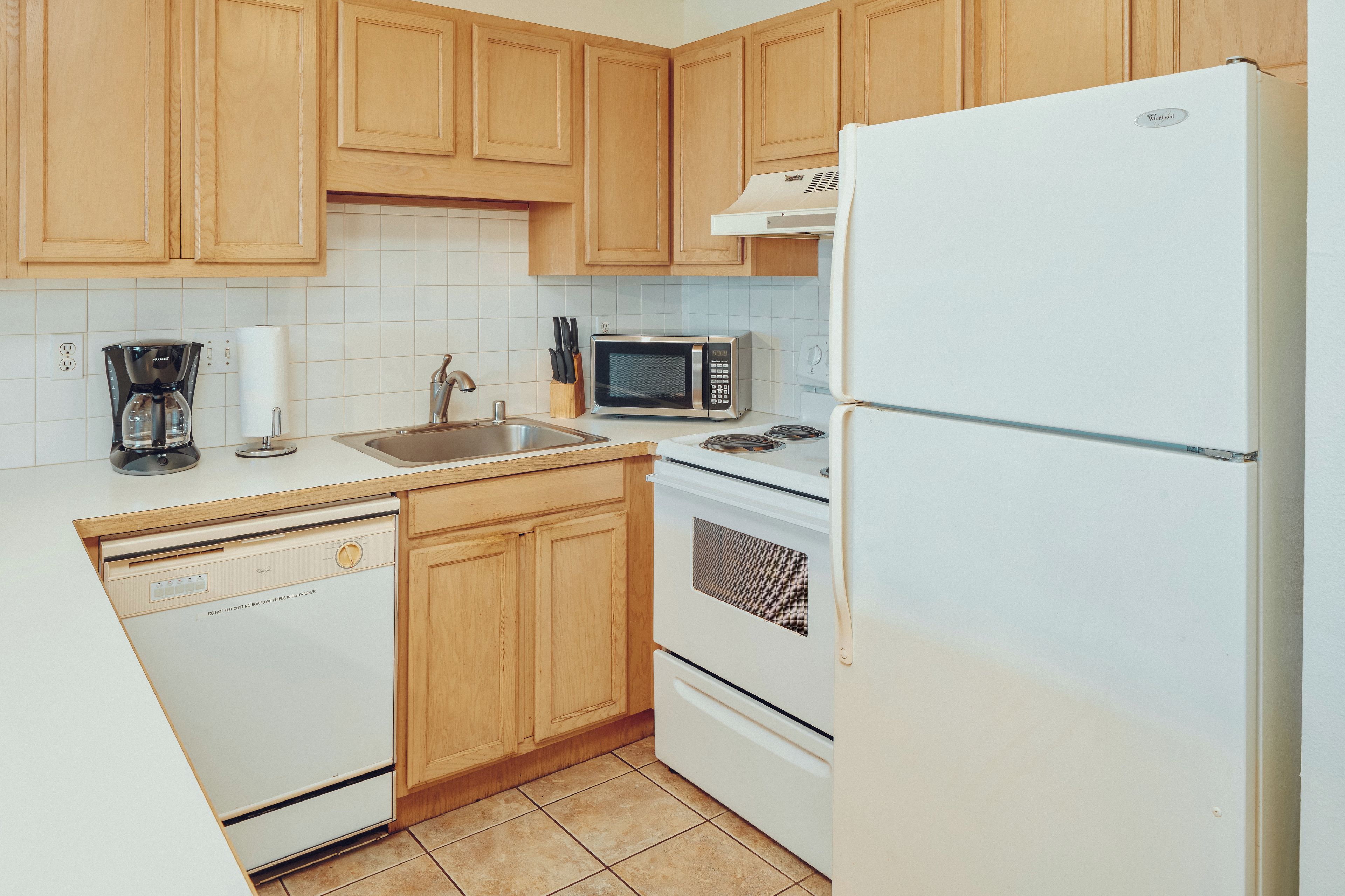 A kitchen with wooden cabinets, a white refrigerator, a microwave, a dishwasher, and a stove.