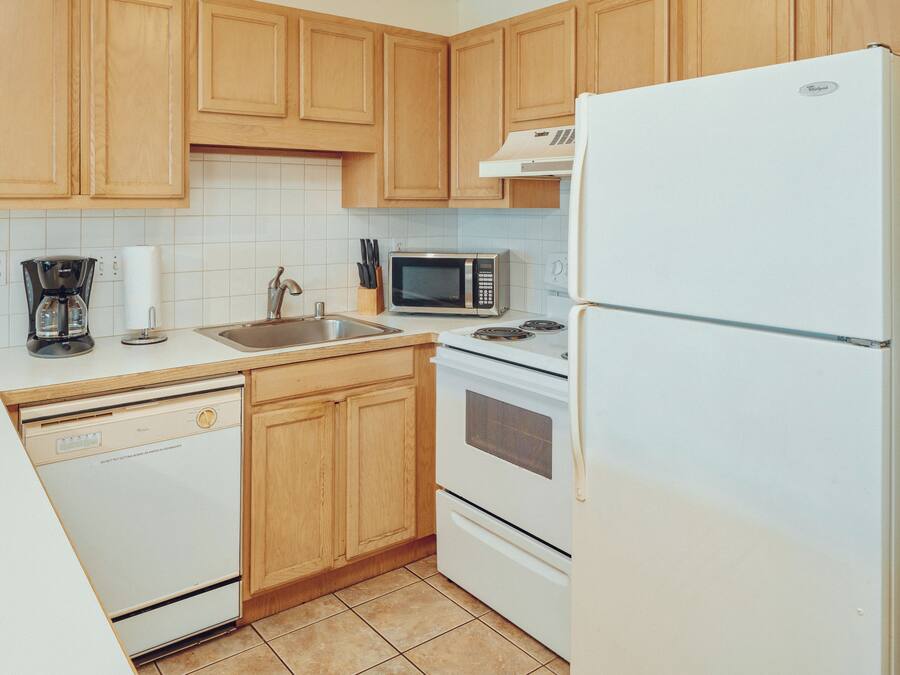 A kitchen with wooden cabinets, a white refrigerator, a microwave, a dishwasher, and a stove.