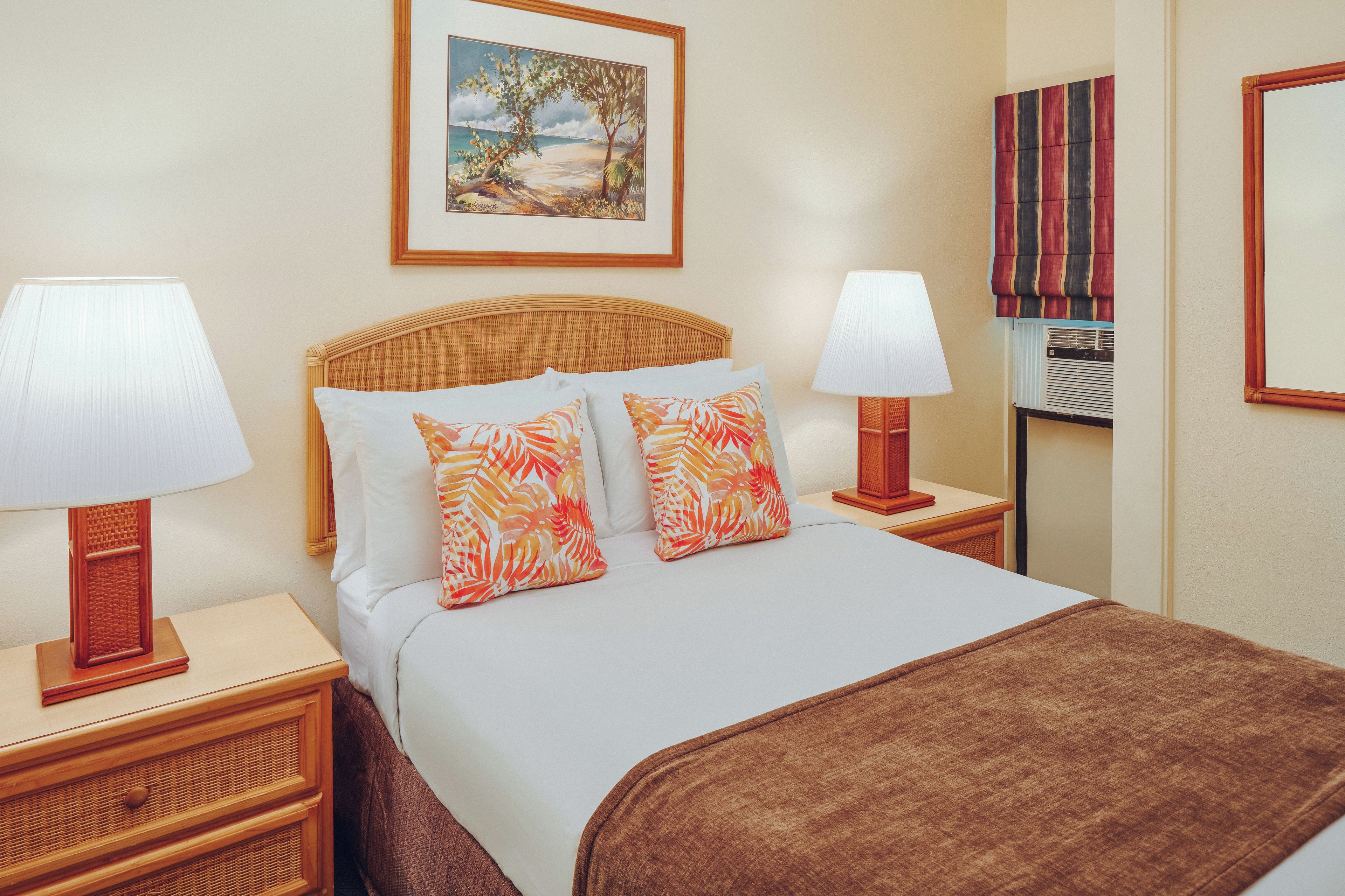 A hotel room with a bed, two nightstands, a lamp, a painting, and a striped curtain.