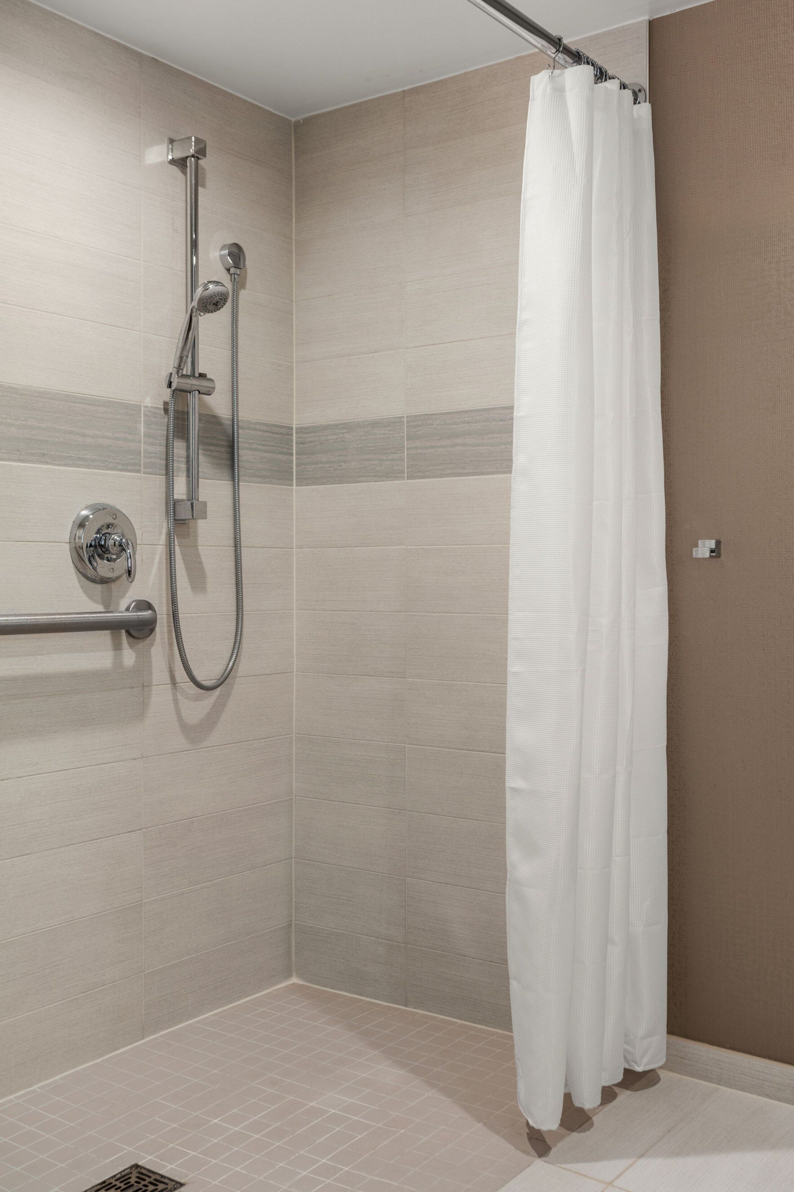 Un espace douche équipé d’un pommeau de douche à main, d’un robinet mural et d’un rideau de douche blanc.