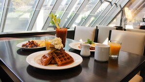 Une table de petit-déjeuner avec des gaufres, un verre de jus d’orange et une carafe de café.