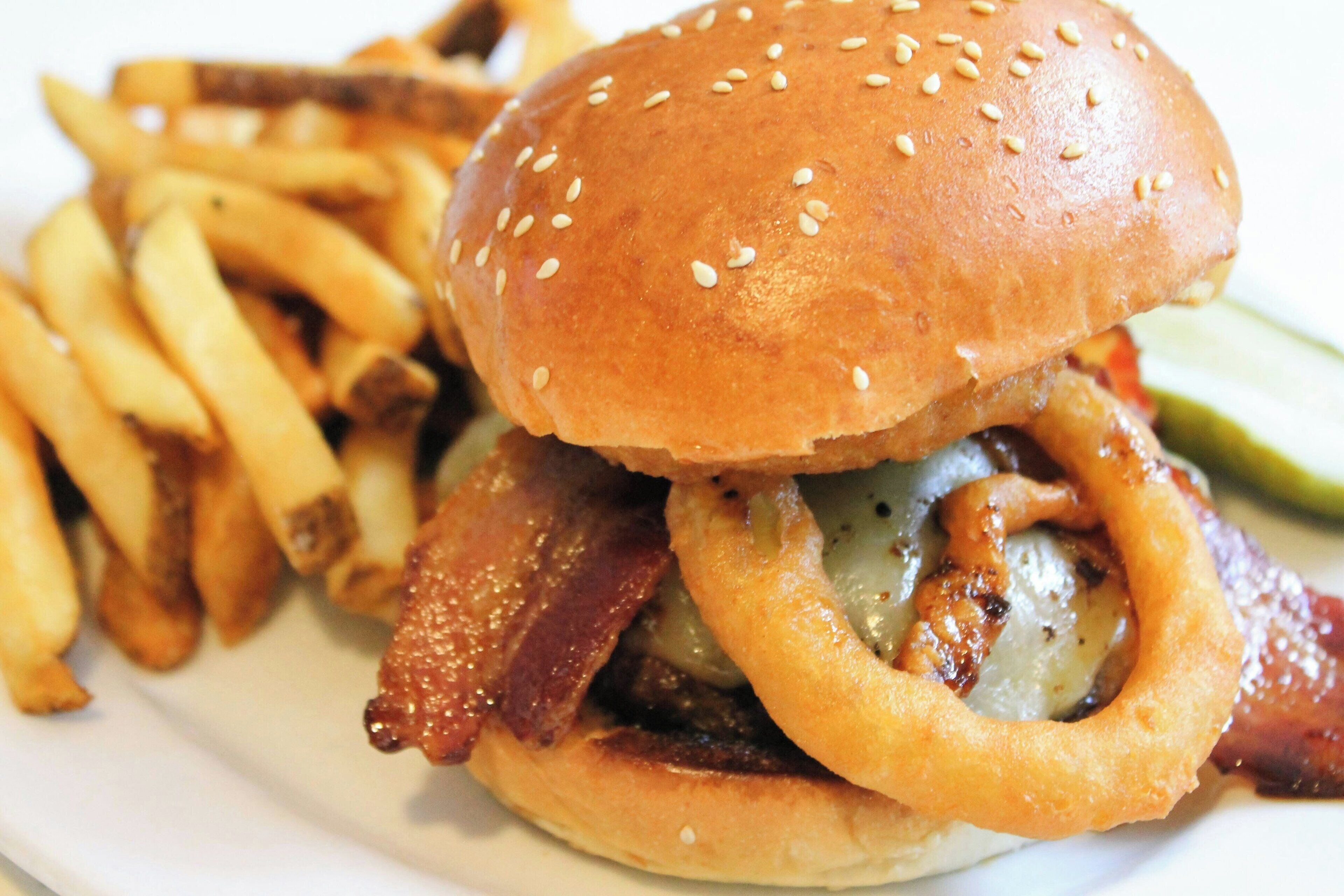 A burger with bacon, cheese, and onion rings, accompanied by French fries.