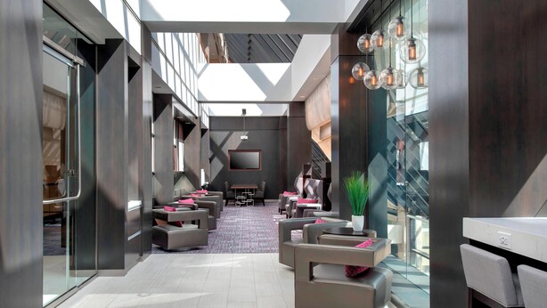 Un hall d’hôtel moderne, doté d’un haut plafond, de murs en verre et d’un espace détente avec des canapés et des fauteuils.