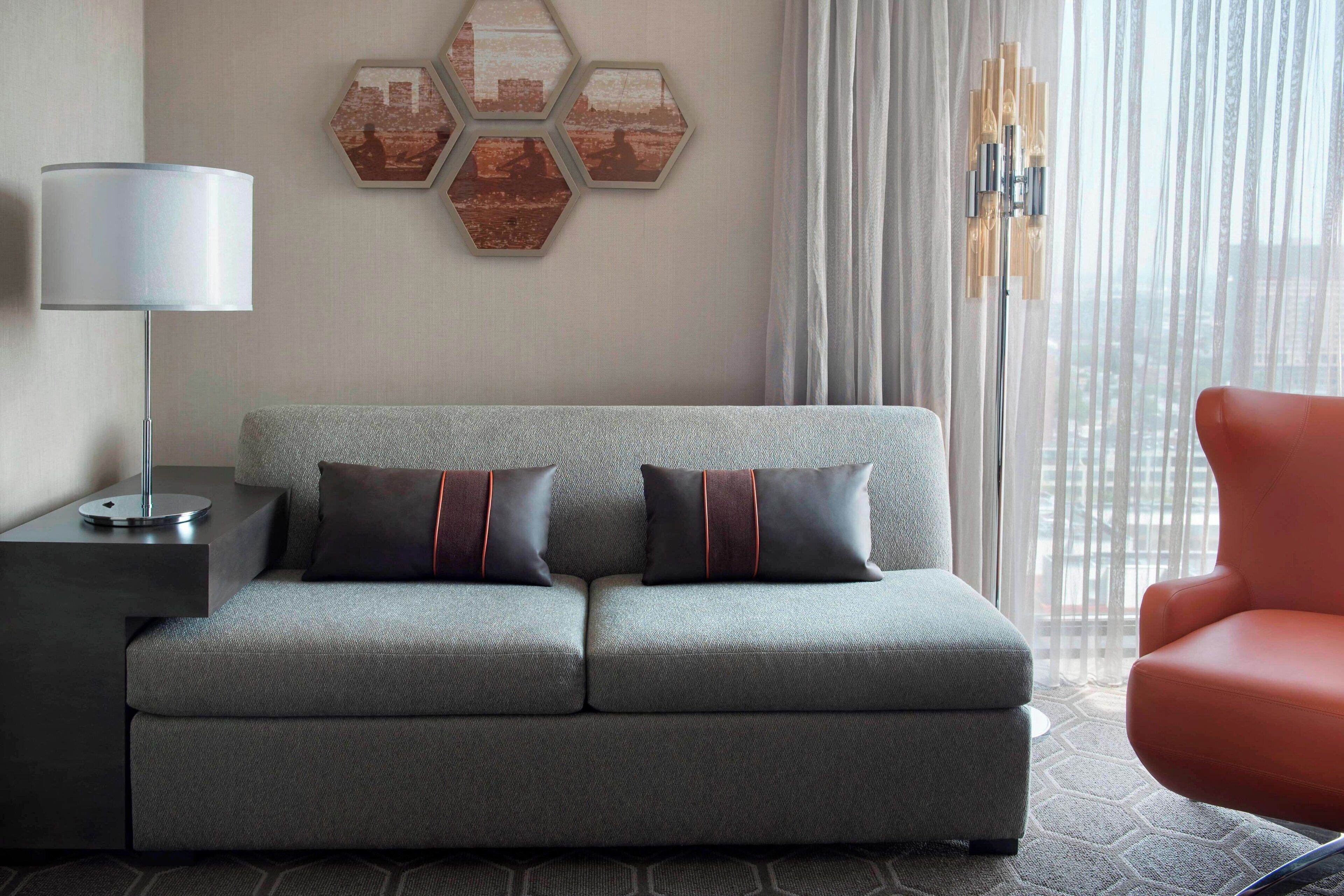 Un salon moderne avec un canapé gris, une table d’appoint, une lampe et un fauteuil rouge.