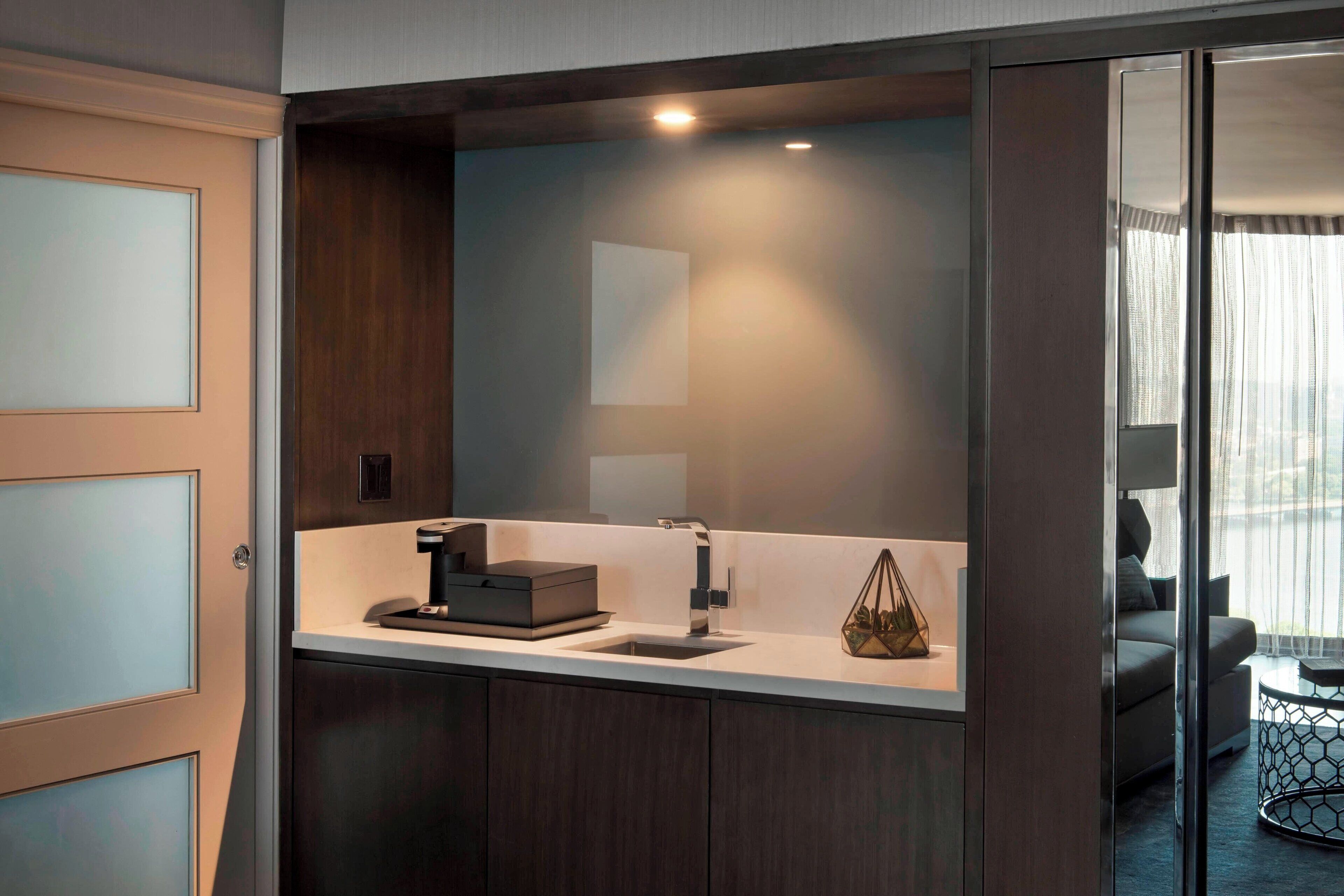Un baño moderno con tocador de madera oscura, un lavabo blanco y una cafetera.