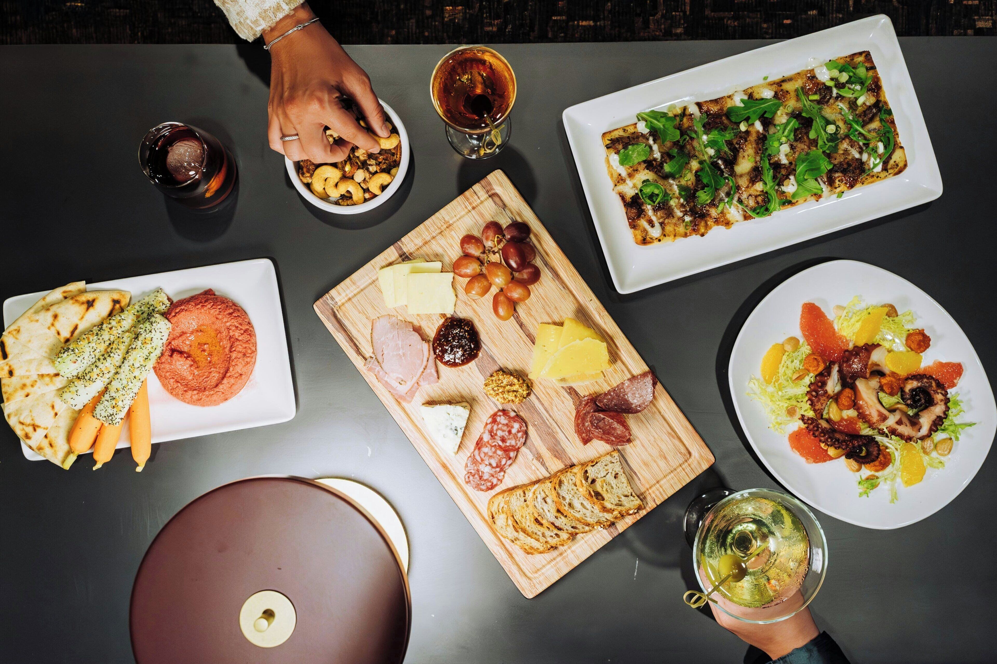 Uma mesa com diversos alimentos, incluindo queijos, carnes e vegetais, além de bebidas.