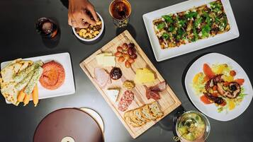Uma mesa com diversos alimentos, incluindo queijos, carnes e vegetais, além de bebidas.