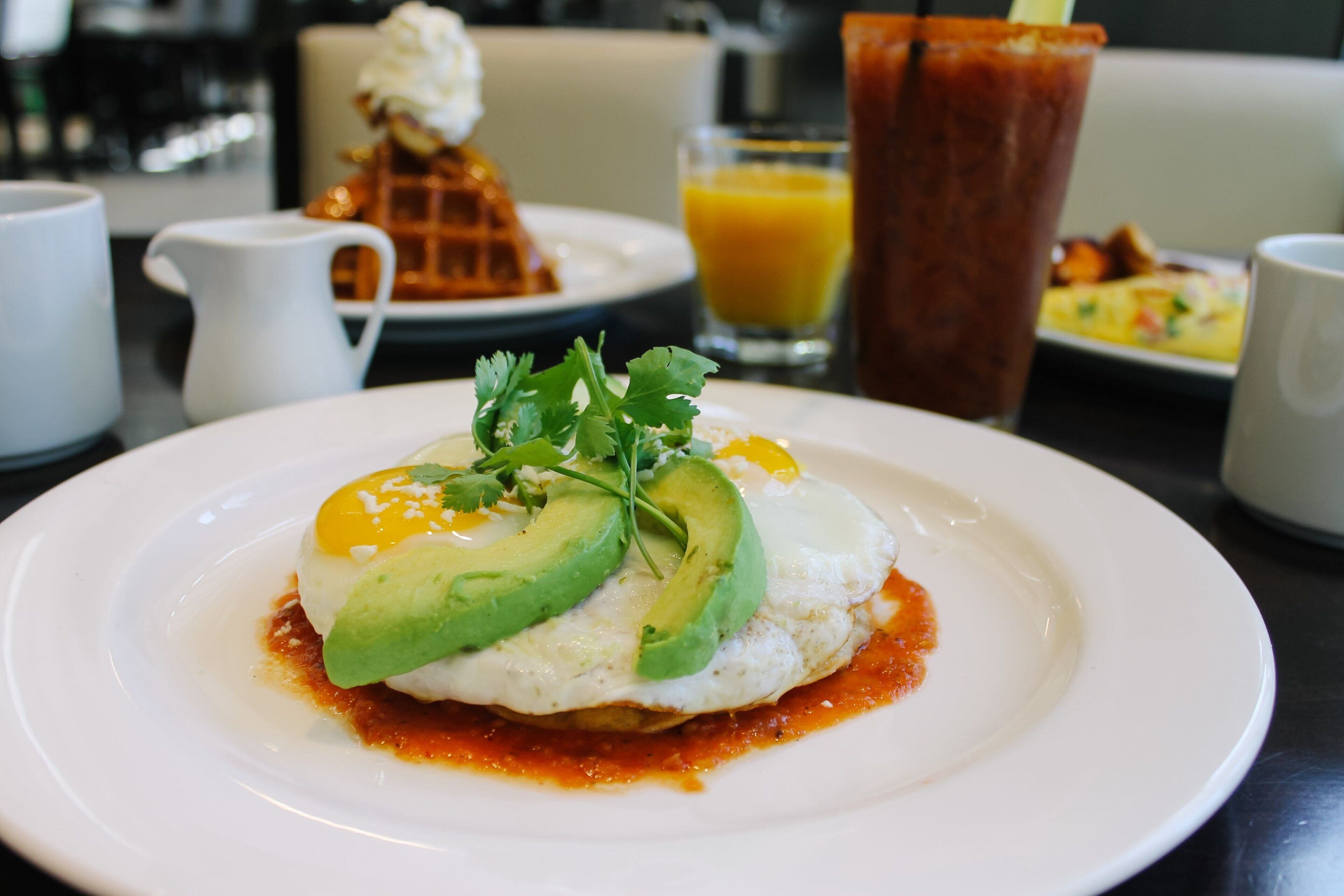 Un plato de desayuno con un huevo, aguacate y salsa, un vaso de zumo de naranja y una jarra de agua sobre una mesa.