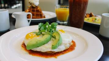Un plato de desayuno con un huevo, aguacate y salsa, un vaso de zumo de naranja y una jarra de agua sobre una mesa.