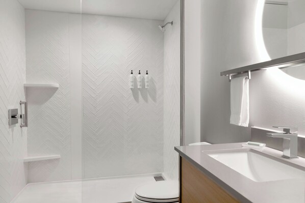 Un baño moderno con ducha de vidrio, un lavamanos blanco y un espejo encima.