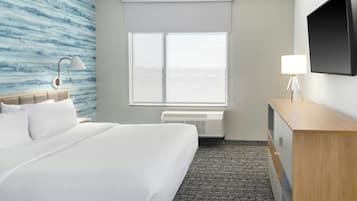 A hotel room with a bed, a desk, a lamp, a flat-screen TV, and a window with a view.