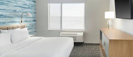 Une chambre d’hôtel équipée d’un lit, d’un bureau, d’une lampe, d’un téléviseur à écran plat et d’une fenêtre donnant sur un paysage agréable.