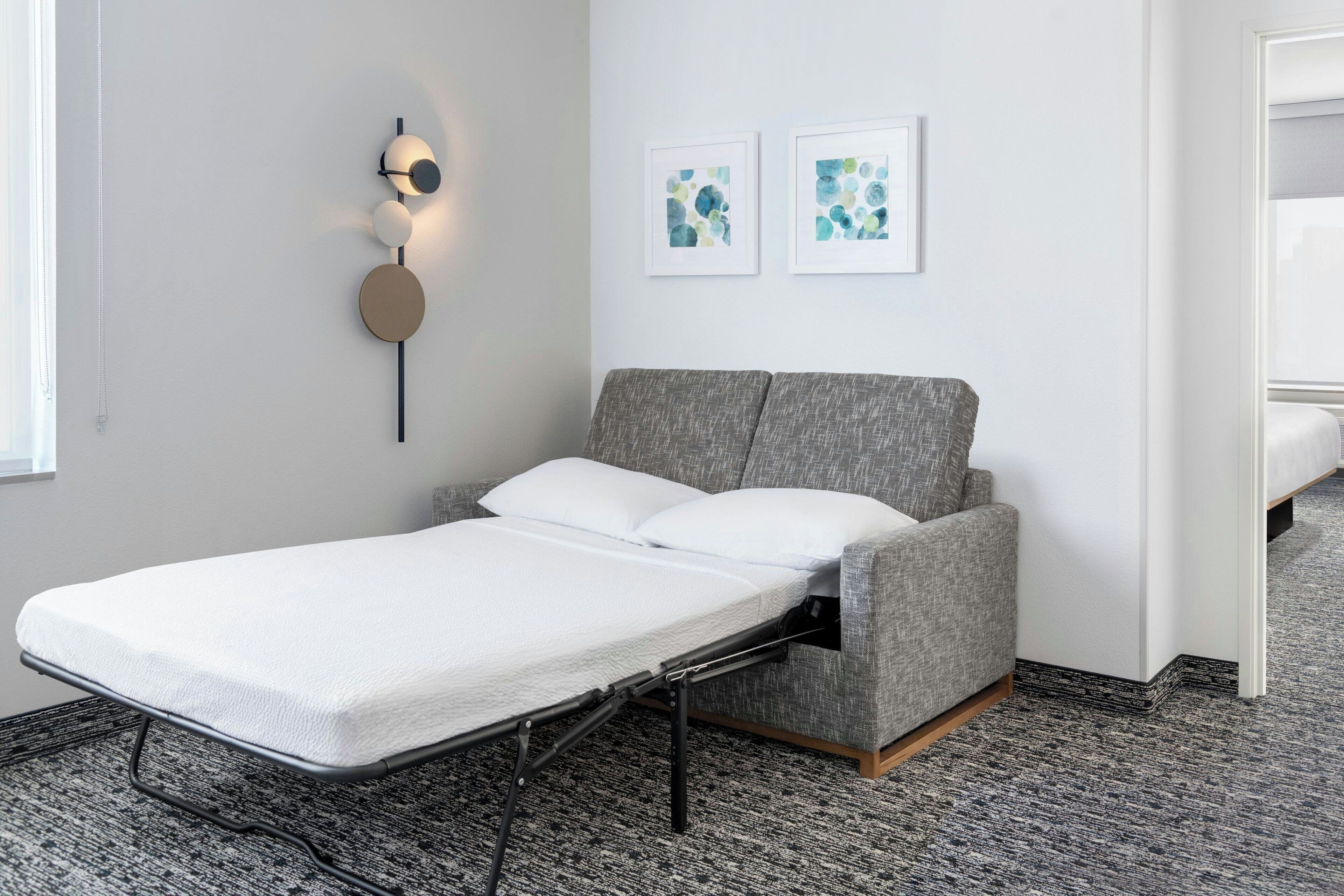 Un letto singolo con una testiera grigia in una stanza con tappeto a motivi, un lampadario a parete e due opere d'arte astratte incorniciate.