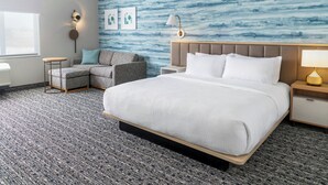 Une chambre d’hôtel avec un grand lit, un canapé gris, une petite table et un mur orné d’un motif abstrait bleu.
