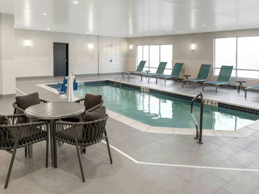 An indoor swimming pool with a lounge area, chairs, and a table.