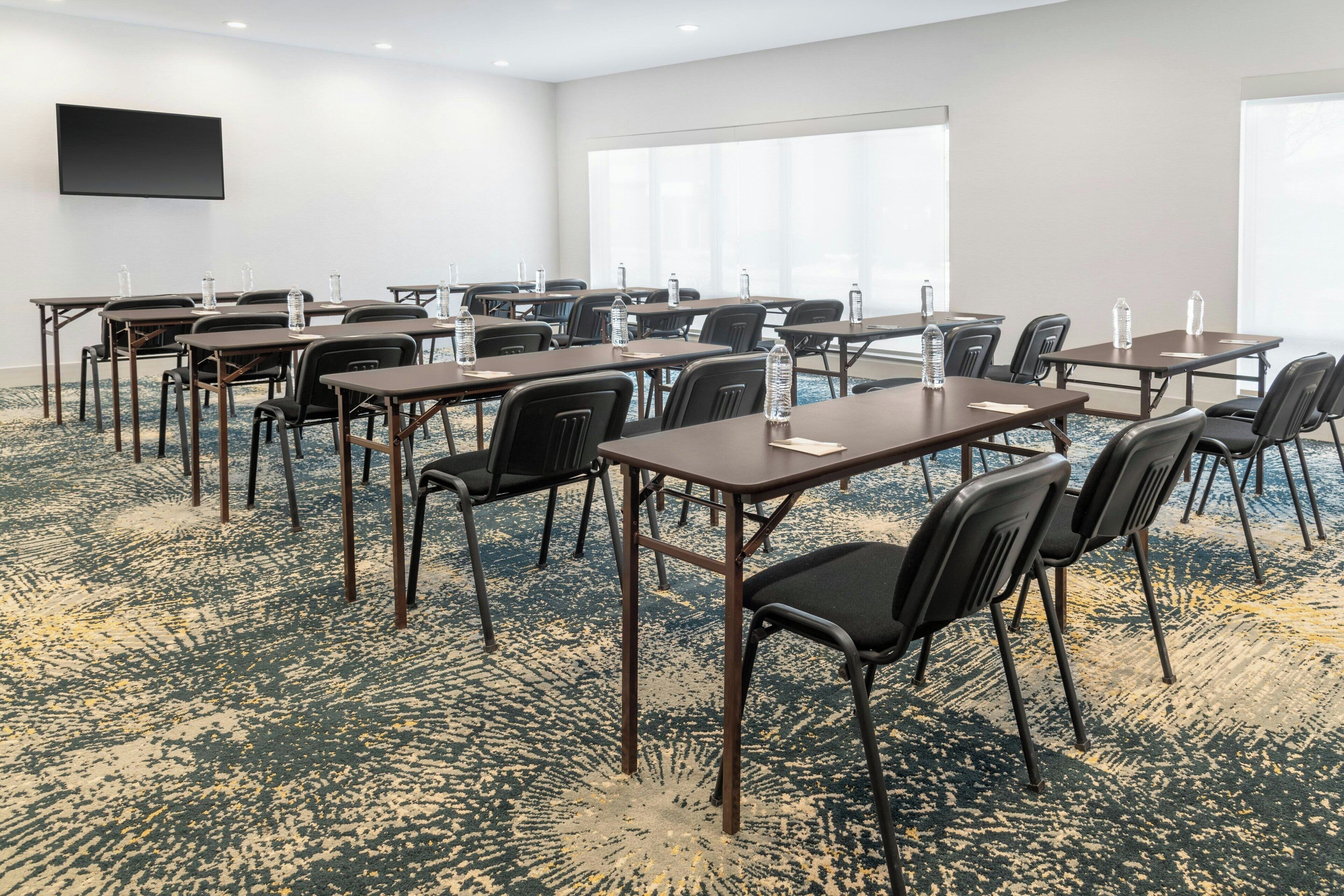 A conference room with tables and chairs, a flat-screen TV, and large windows.