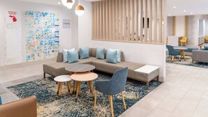 Un hall d’hôtel moderne avec un canapé modulable, des tables rondes et un mur décoratif orné d’œuvres d’art abstraites.