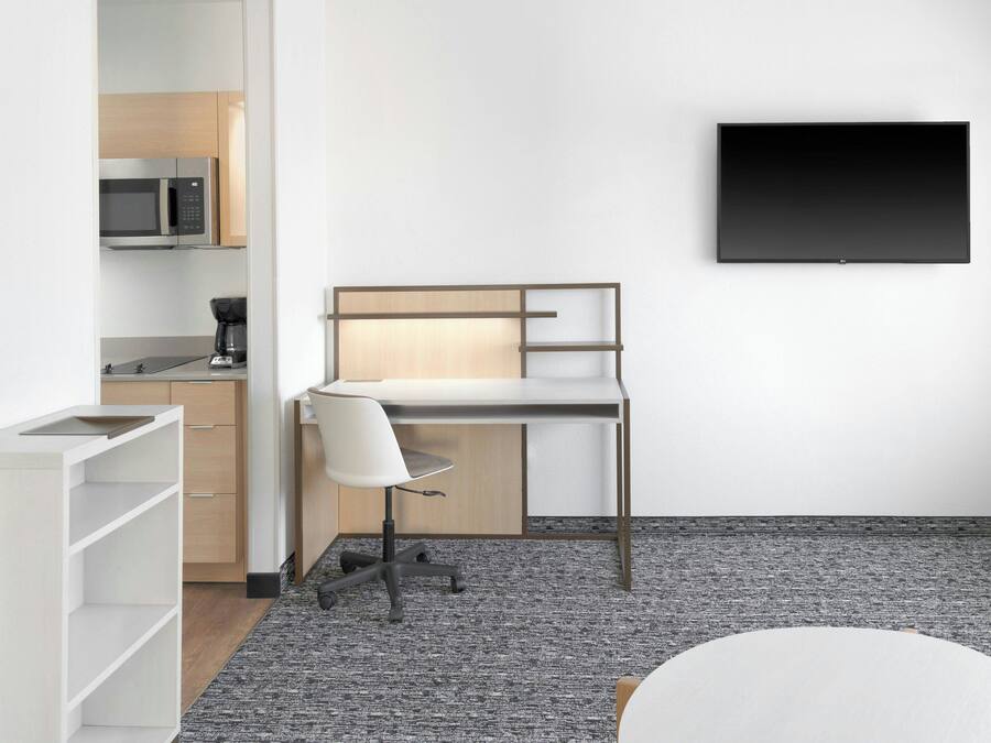 A modern office space with a desk, chair, and a flat-screen TV mounted on the wall.