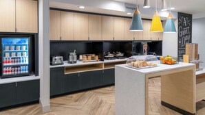 Une cuisine moderne avec des meubles en bois, un réfrigérateur rempli de boissons et un bar pour prendre le petit-déjeuner, où sont servis des viennoiseries.