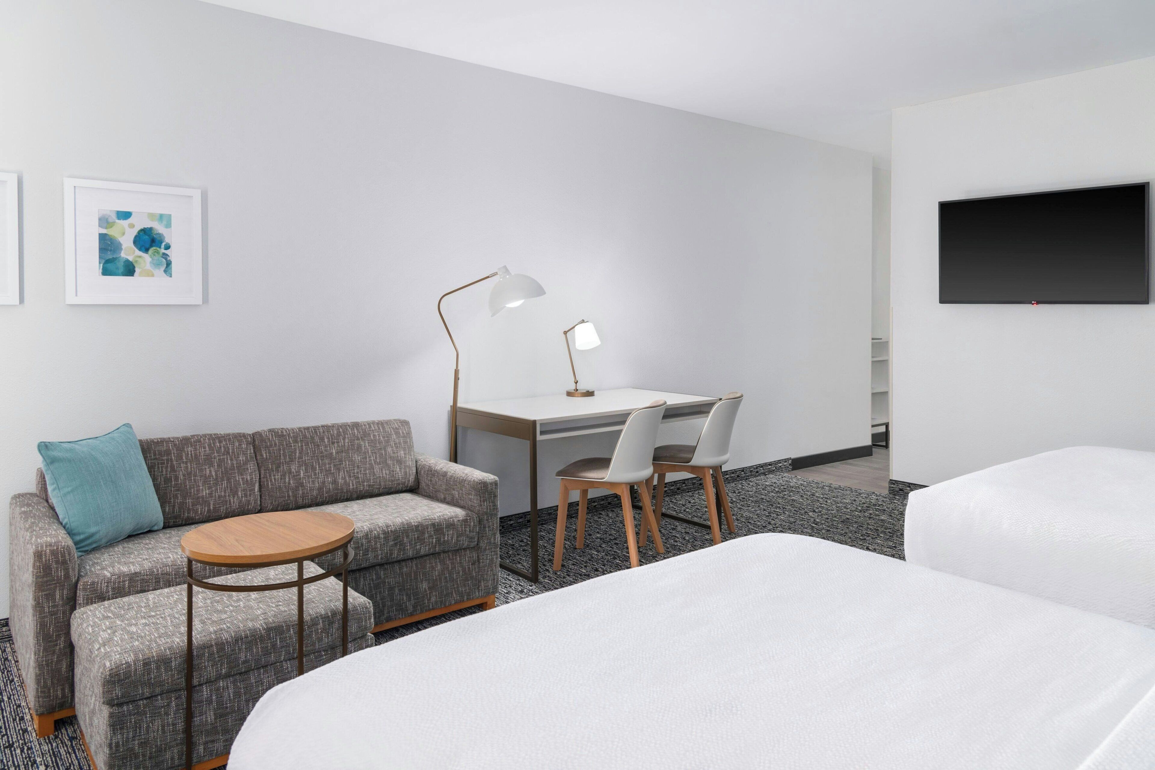 Habitación de hotel con sofá, dos sillones, escritorio, lámpara, televisor y dos camas.