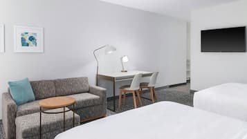 Habitación de hotel con sofá, dos sillones, escritorio, lámpara, televisor y dos camas.