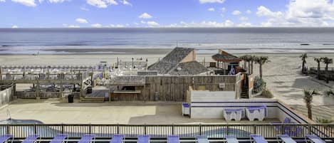 A beachside hotel with a pool, sun loungers, and a wooden deck overlooking the ocean.