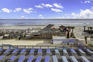 Un hotel frente a la playa con piscina, tumbonas y una terraza de madera con vistas al océano.