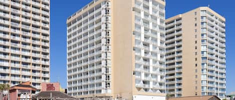 Un hotel frente a la playa con varios edificios de gran altura, un paseo marítimo y una playa en primer plano.