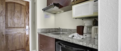 A kitchen with a wooden door, granite countertop, stainless steel sink, and a dishwasher.