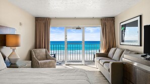 A hotel room with a bed, two armchairs, a sofa, a desk, and a large window with a view of the beach and ocean. - Seahaven Beach Hotel (Panama City Beach)