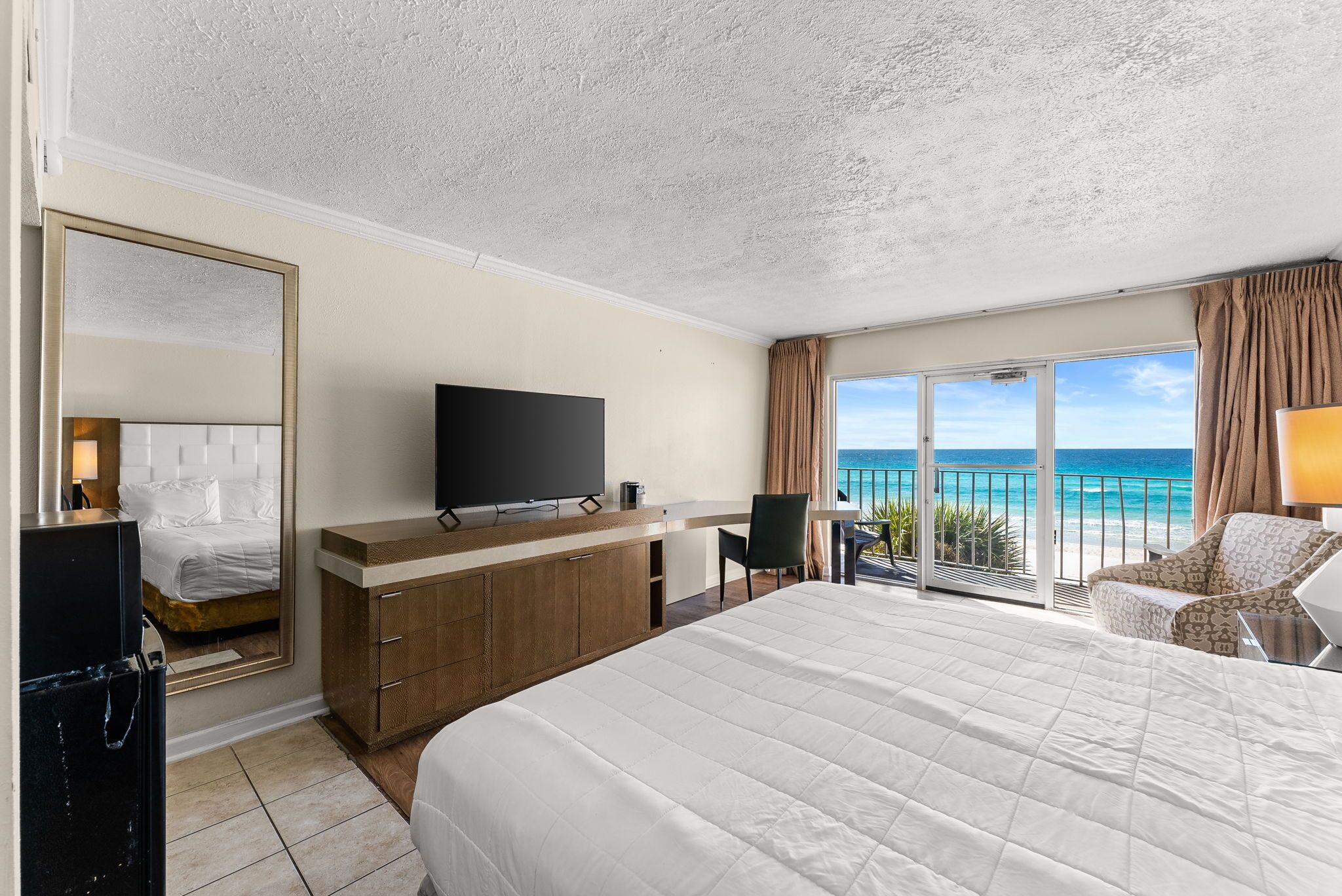 Una habitación de hotel con una cama grande, televisión, escritorio y vista al océano.