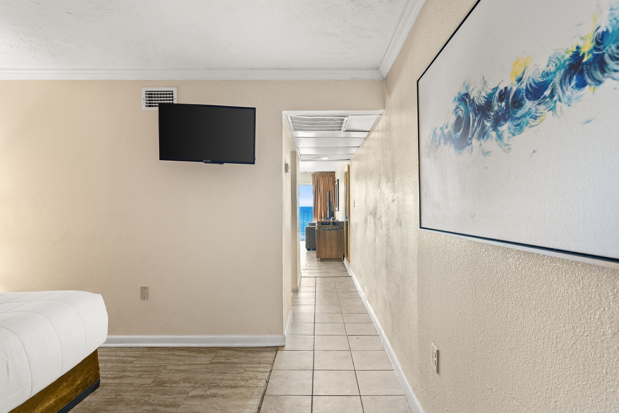 Quarto de hotel com uma cama, televisão de tela plana na parede e um quadro na parede.