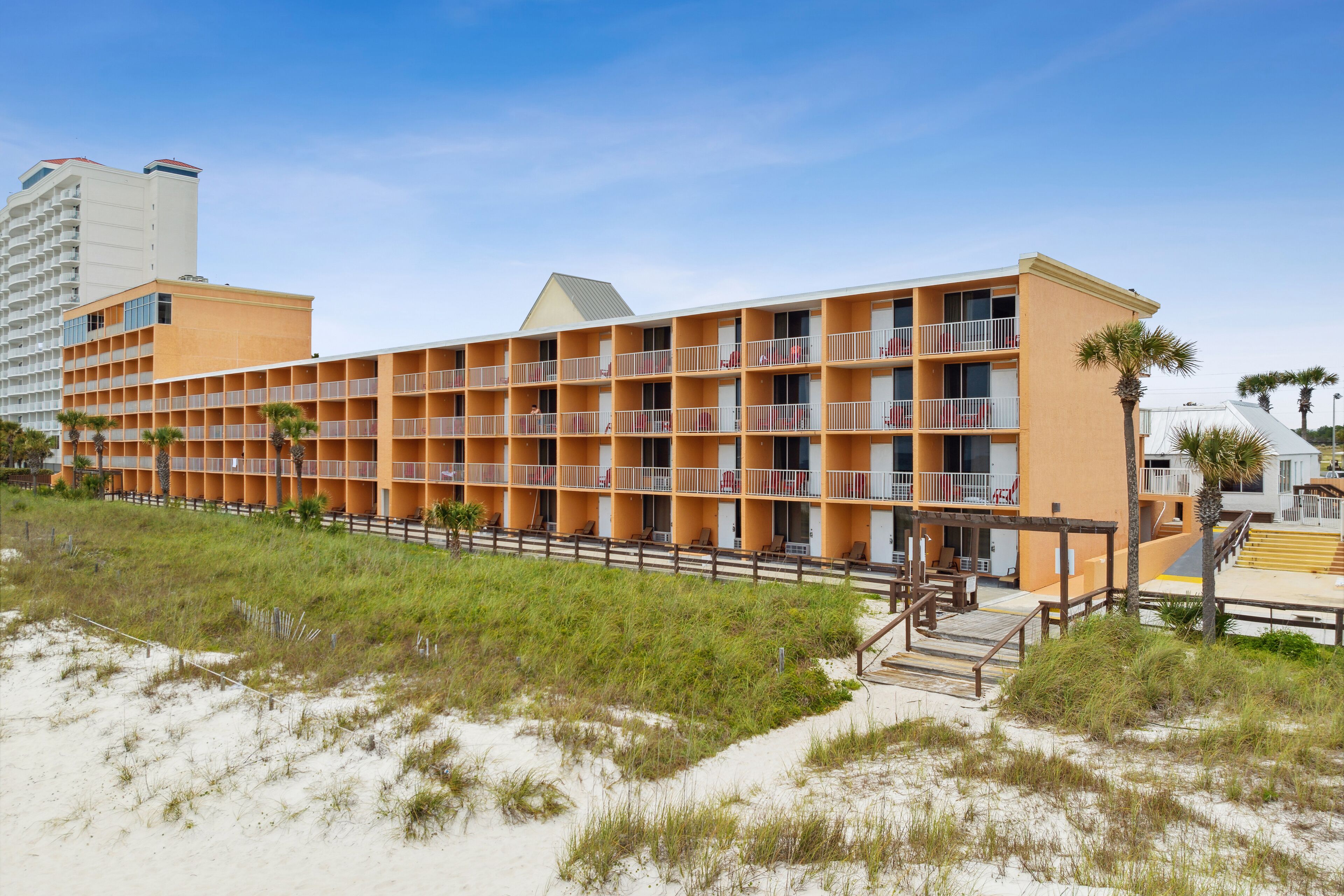 A beachfront hotel with multiple balconies, a sandy beach in front, and a clear sky.