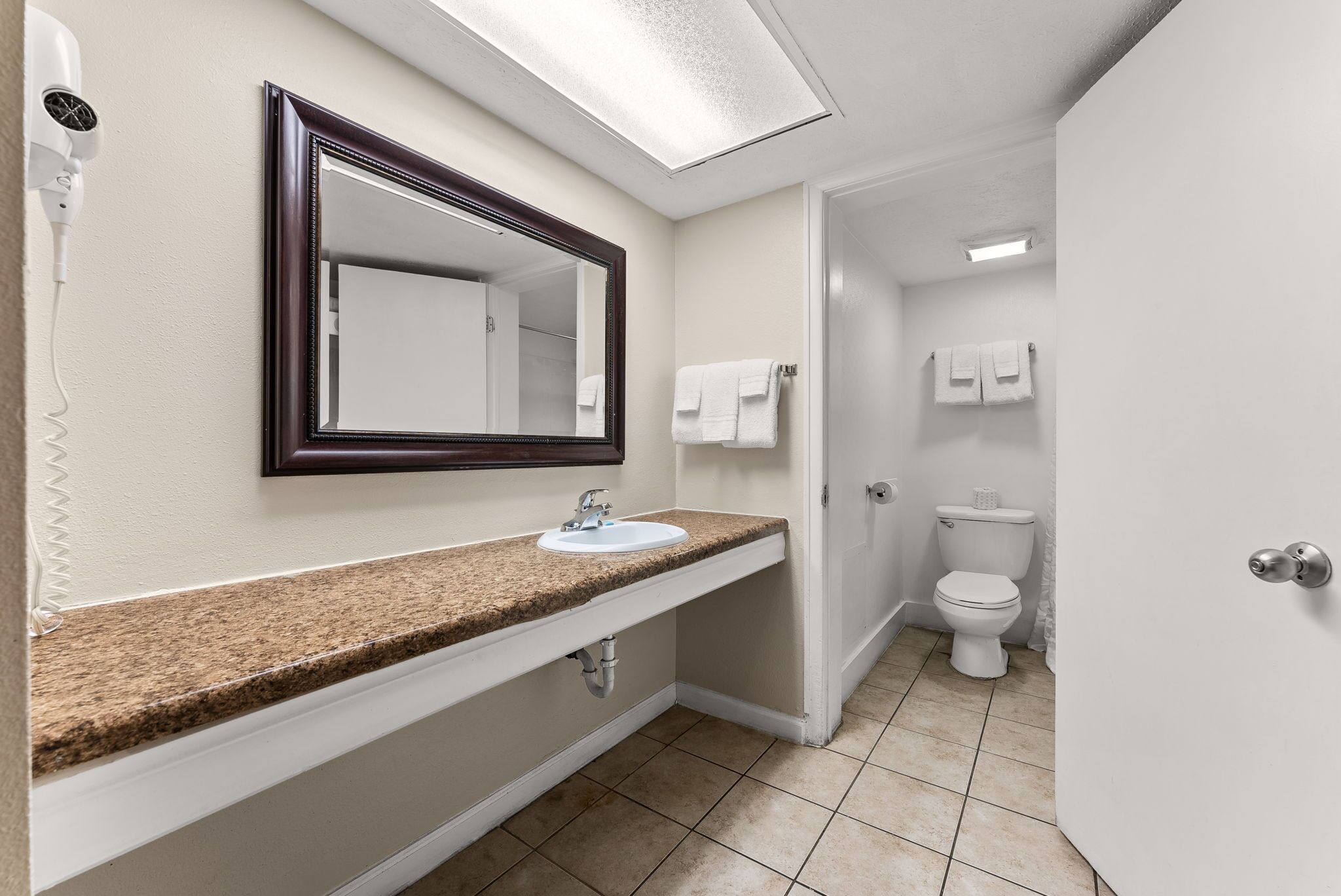A bathroom with a granite countertop sink, a mirror, a hairdryer, and a toilet.