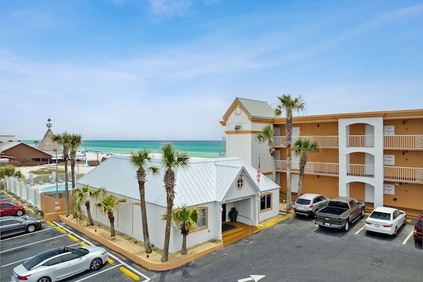Hotel com piscina, vista para a praia e estacionamento com vários carros.