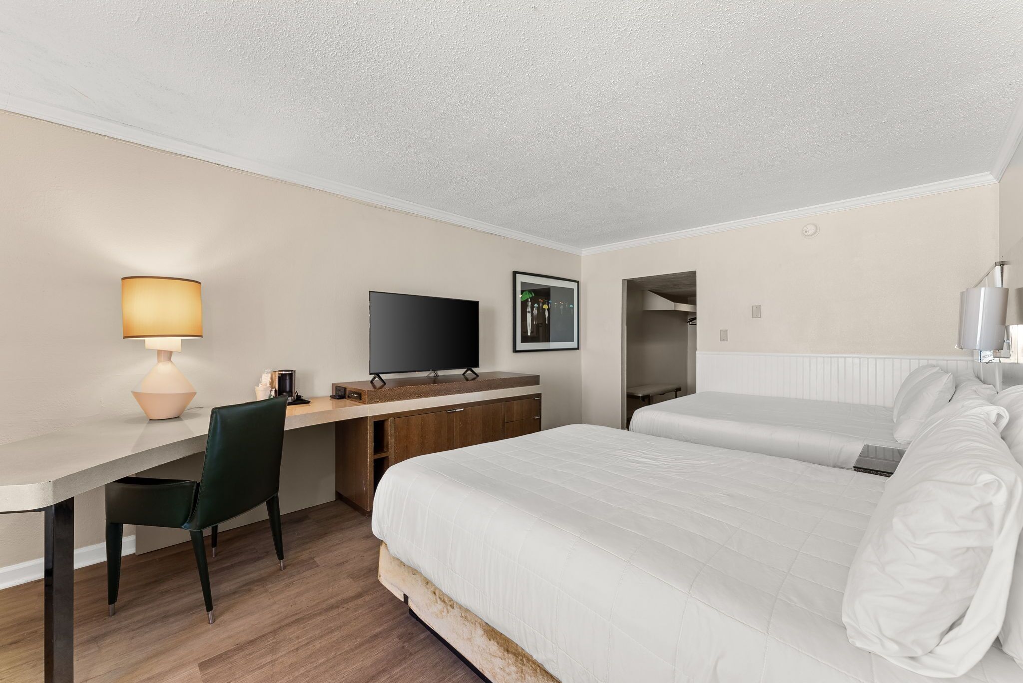 A hotel room with a bed, a desk with a chair, a television, and a lamp.