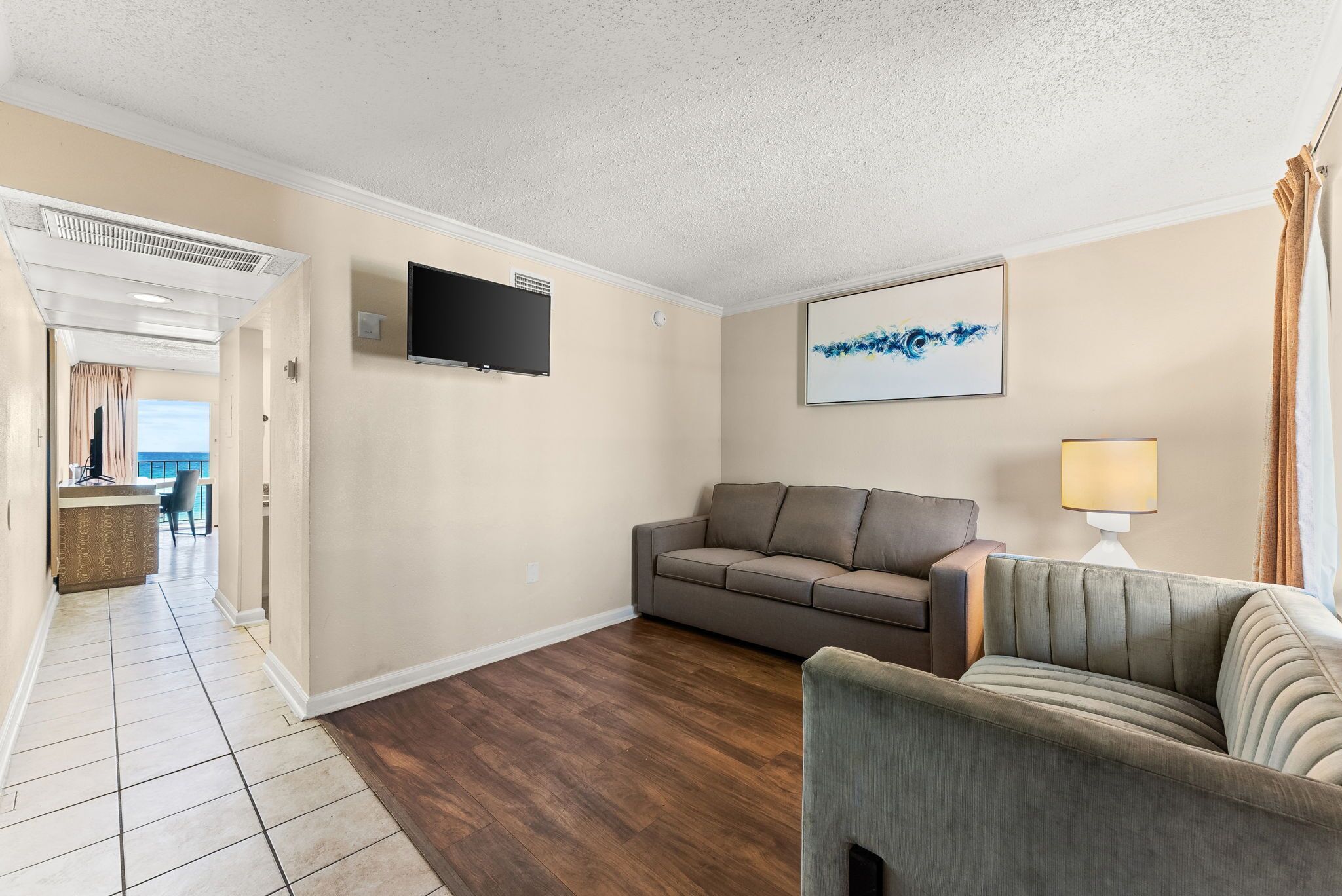 A living room with a sofa, a TV mounted on the wall, and a lamp.