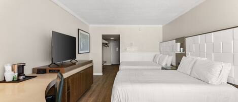 A hotel room with a bed, a TV, a desk with a coffee maker, and a view of the hallway.