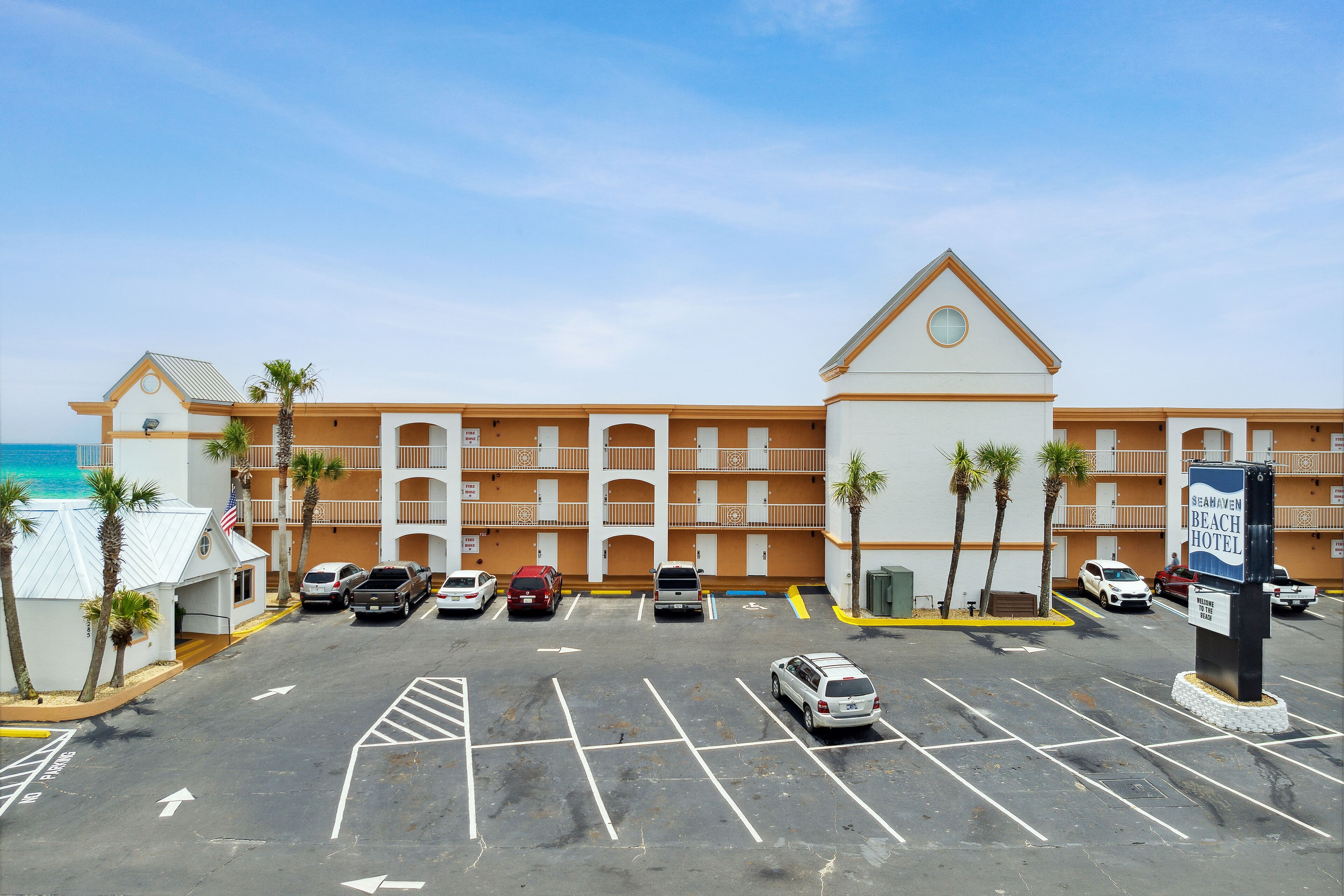 A beachfront hotel with a parking lot, multiple floors, and a view of the ocean.