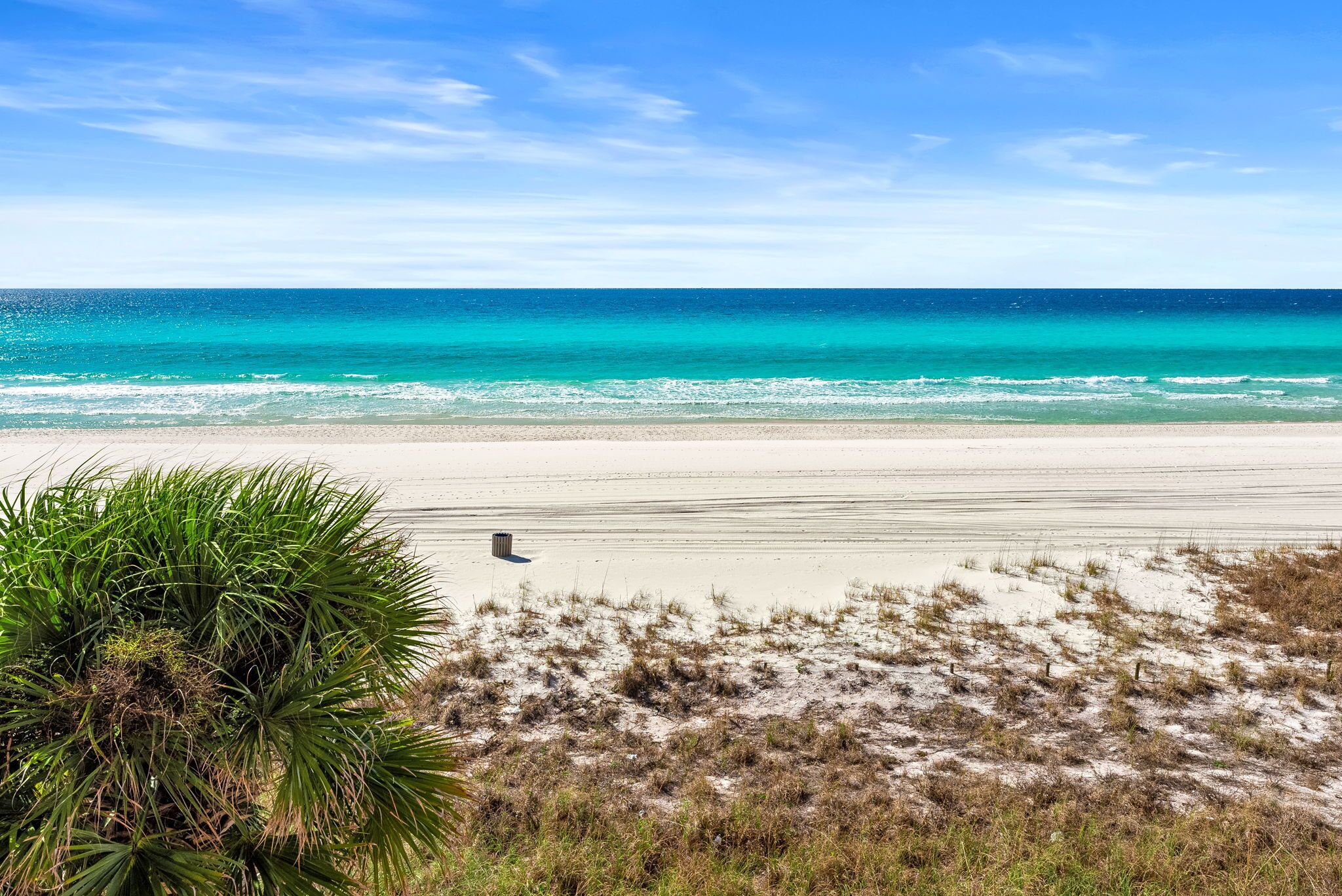 Una playa con agua turquesa cristalina, orilla arenosa y vegetación escasa.