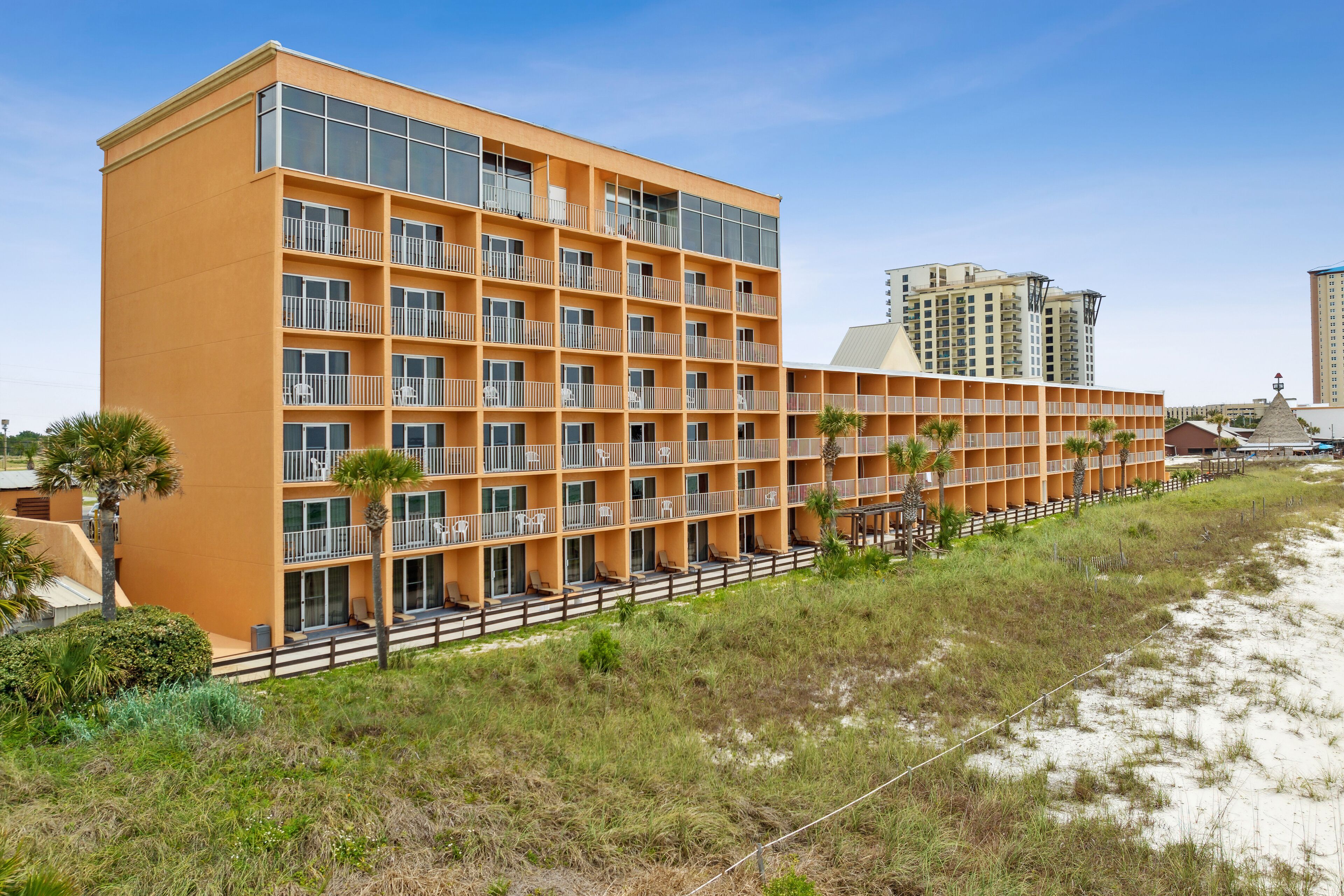Un hôtel à plusieurs étages doté de balcons, situé près d’une plage de sable et d’herbe.
