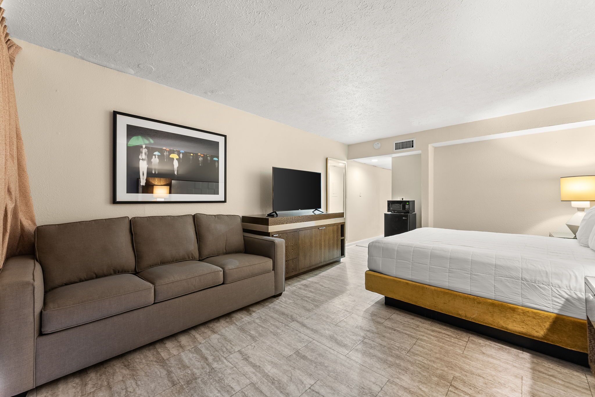 Ein Hotelzimmer mit einer Couch, einem Bett, einem Fernseher, einer Kaffeemaschine und einem gerahmten Bild an der Wand.