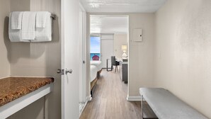 A hotel room with a bathroom, a bed, a bench, and a view of the outside. - Seahaven Beach Hotel (Panama City Beach)