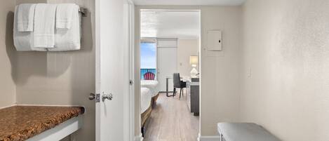 A hotel room with a bathroom, a bed, a bench, and a view of the outside.