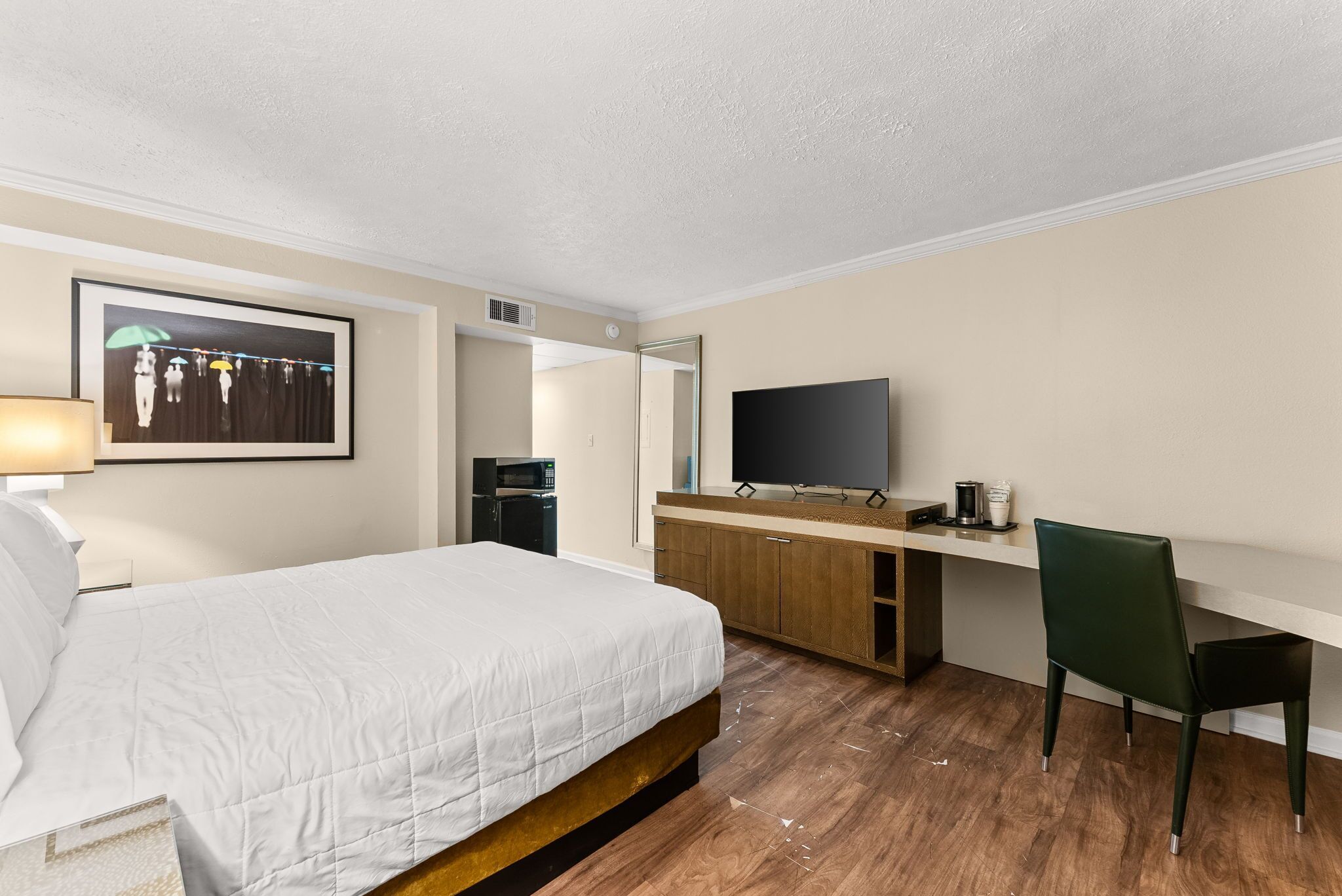 A hotel room with a bed, a desk with a chair, a flat-screen TV, a microwave, and a framed picture on the wall.