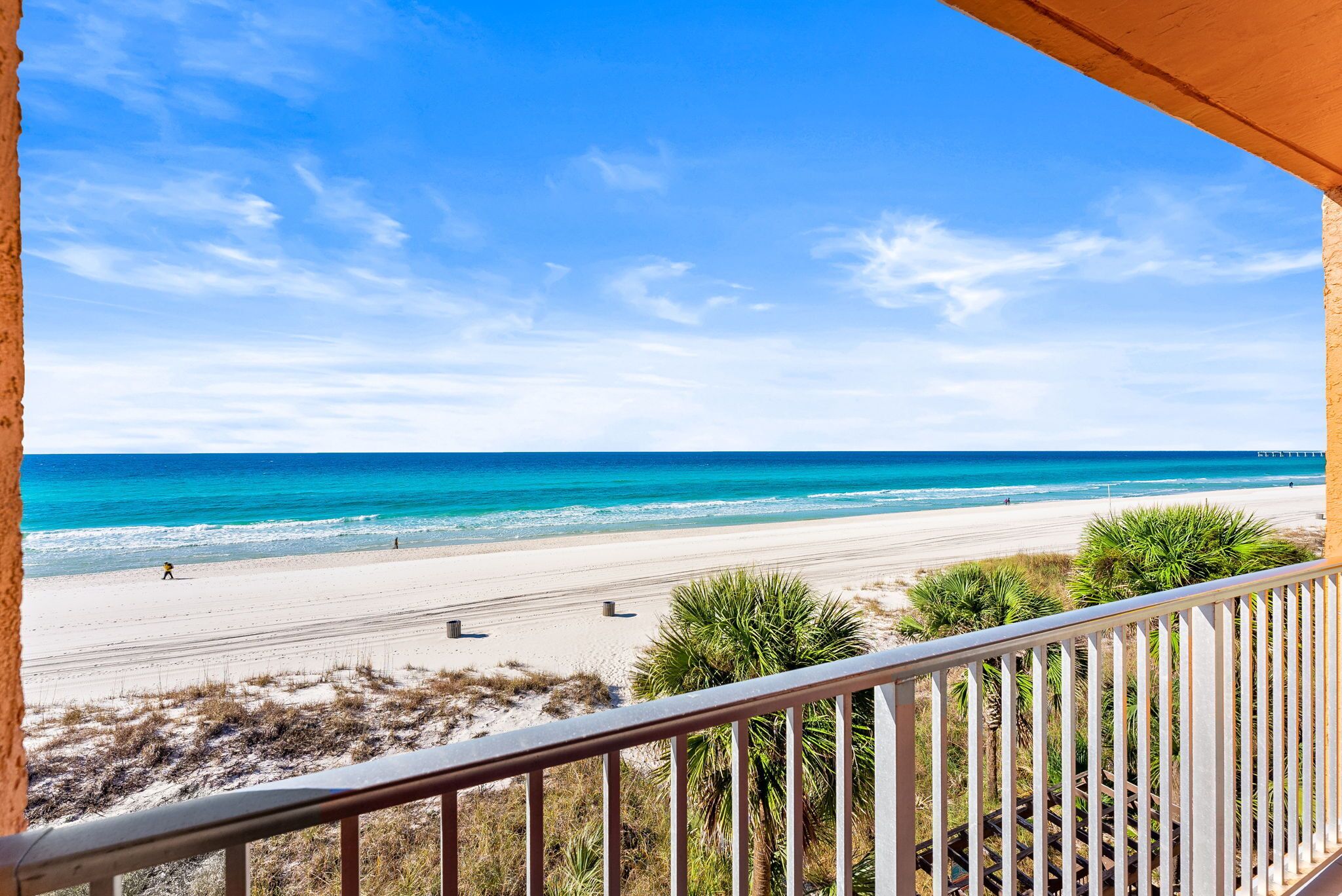 A beach view from a balcony with a railing, sandy beach, and ocean.